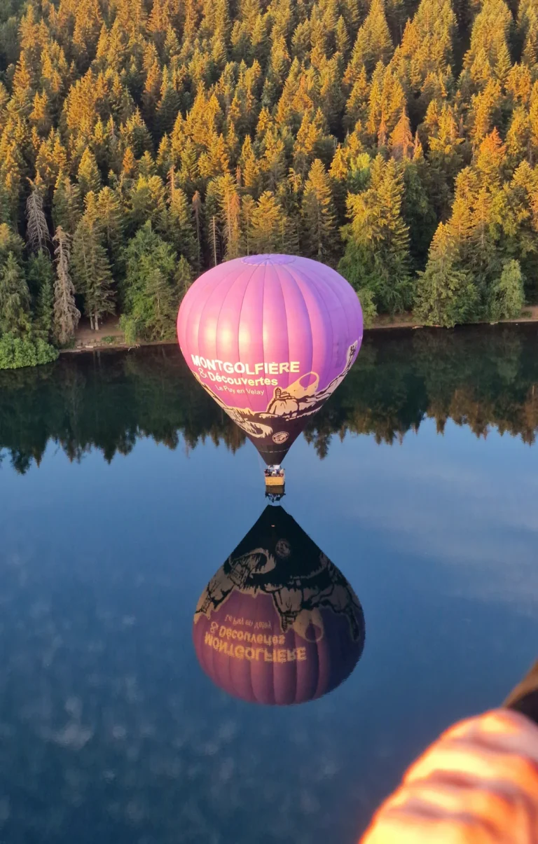 Montgolfière violette et son reflet sur un lac entouré de forêt